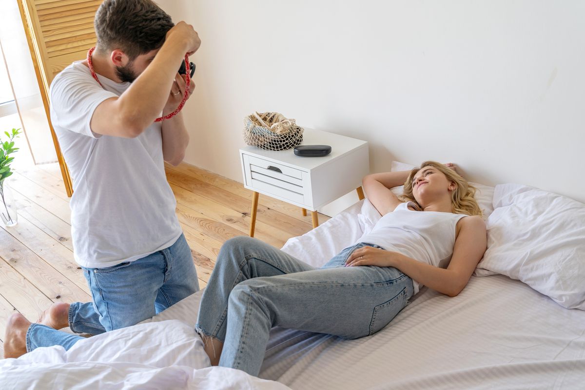 Pretty young woman posing fot camera in bedBearded man photographing girlfriend in bedroom stock photoBearded man photographing girlfriend in bedroom stock photo