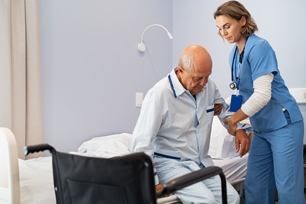 Lovely,Nurse,Assisting,Senior,Man,To,Get,Up,From,Bed