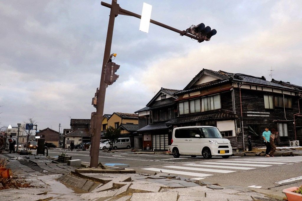 A car drives past a badly damaged pavement along a street in the city of Wajima, Ishikawa prefecture on January 1, 2024, after a major 7.5 magnitude earthquake struck the Noto region in Ishikawa prefecture in the afternoon. Tsunami waves over a metre high hit central Japan on January 1 after a series of powerful earthquakes that damaged homes, closed highways and prompted authorities to urge people to run to higher ground. (Photo by Yusuke FUKUHARA / Yomiuri Shimbun / AFP) / Japan OUT / NO ARCHIVES - MANDATORY CREDIT: Yomiuri Shimbun