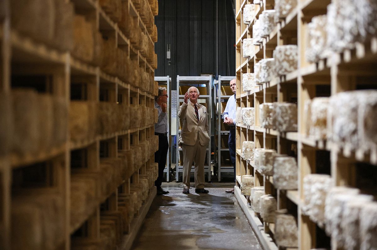 Britain's King Charles III (C) looks at the cheeses displayed on shelves in storage room during a visit of the Lincolnshire Poacher Cheese farm, in Ulceby, England, on July 24, 2023. The farm began dairying in 1970 with Simon’s father, Richard, but it wasn’t until Simon came back from agricultural college that he began exploring the possibility of making cheese at the farm. Today, all the milk produced on the farm, apart from a small quantity bottled and sold at Farmers Markets, is turned into Lincolnshire Poacher Cheese. (Photo by Cameron Smith / POOL / AFP)