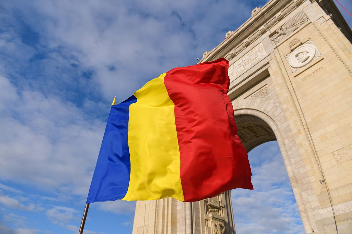 The,National,Flag,Of,Romania,Winding,Next,To,Arch,Of
The national flag of Romania winding next to Arch of Triumph landmark building from Bucharest during a sunny day., román, 