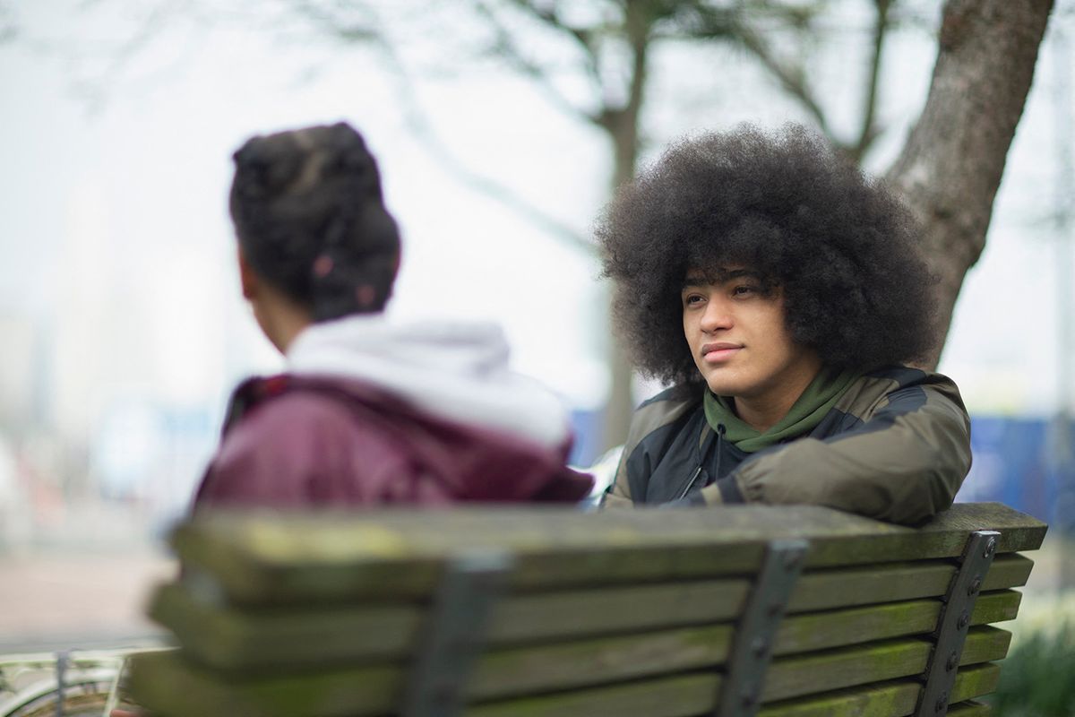 Young man talking to sister on park bench