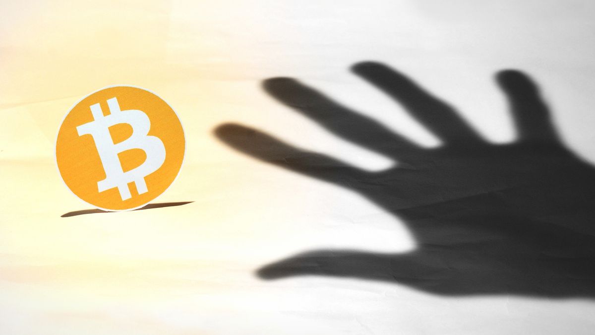 shadow of a hand reaching for bitcoin