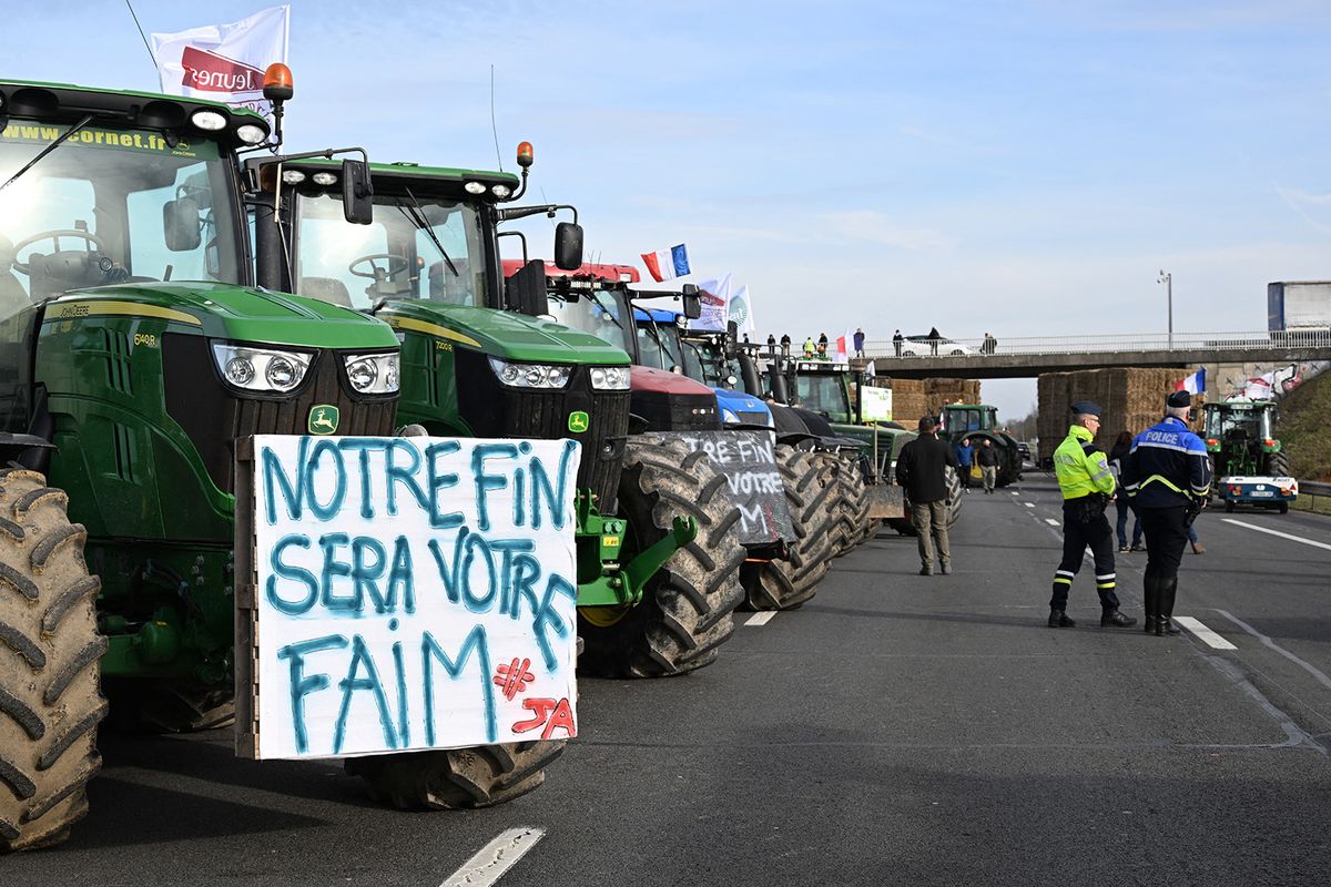 French police stand next to tractors including one with a placard reading "our end will be your hunger" as French farmers take part in a road block protest on the A4 highway near Jossigny, east of Paris, on January 29, 2024, amid nationwide protests called by several farmers unions on pay, tax and regulations. Local branches of major farmer unions FNSEA and Jeunes Agriculteurs announced on January 27, 2024, a "siege of the capital for an indefinite period" starting at 2 p.m. on January 29, 2024, as some farmers feel that the government's announcements in favor of the sector are insufficient. (Photo by Bertrand GUAY / AFP)