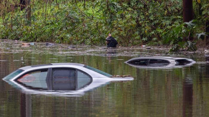A man swims chest-deep through flood waters with his cell phone near three cars that are submerged after rain flooded several areas of Long Beach from the first in a series of storms hits Southern California