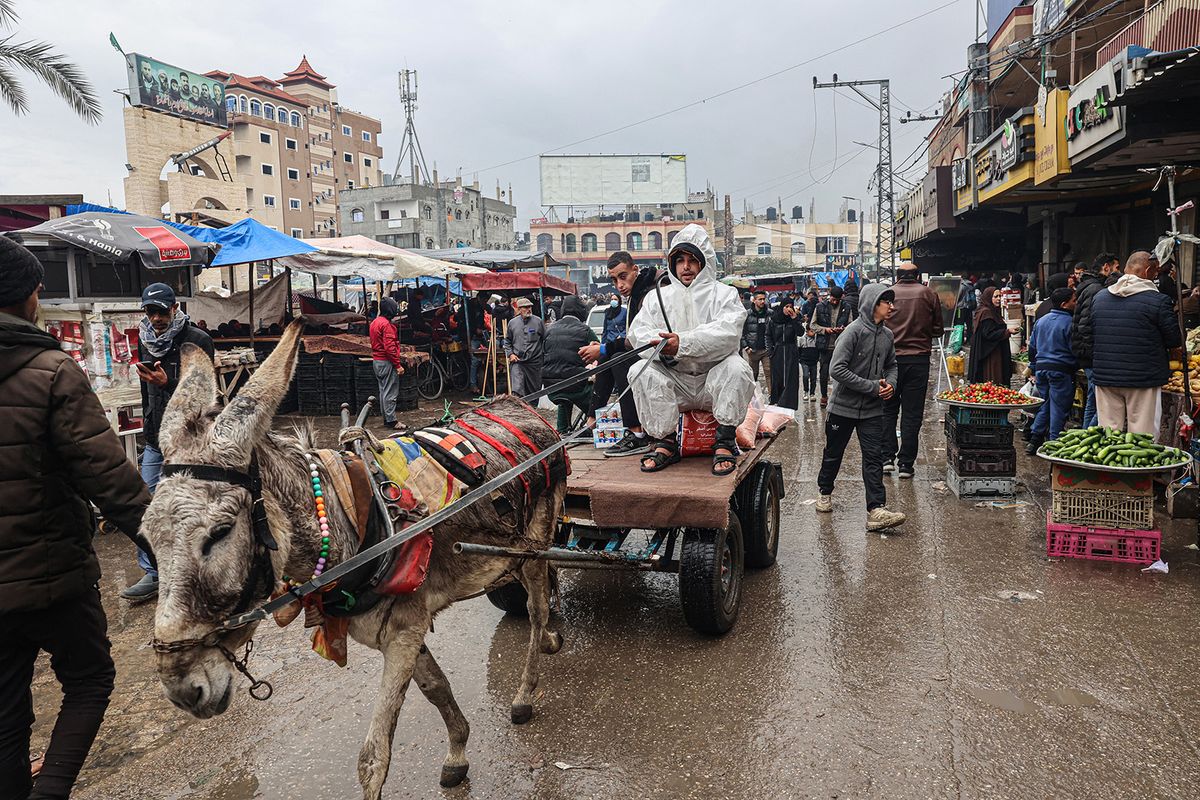 A man wearing a hazmat suit to keep warm, rides a donkey-pulled cart at a market in Rafah in the southern Gaza Strip on February 18, 2024, amid continuing battles between Israel and the militant group Hamas. (Photo by SAID KHATIB / AFP)