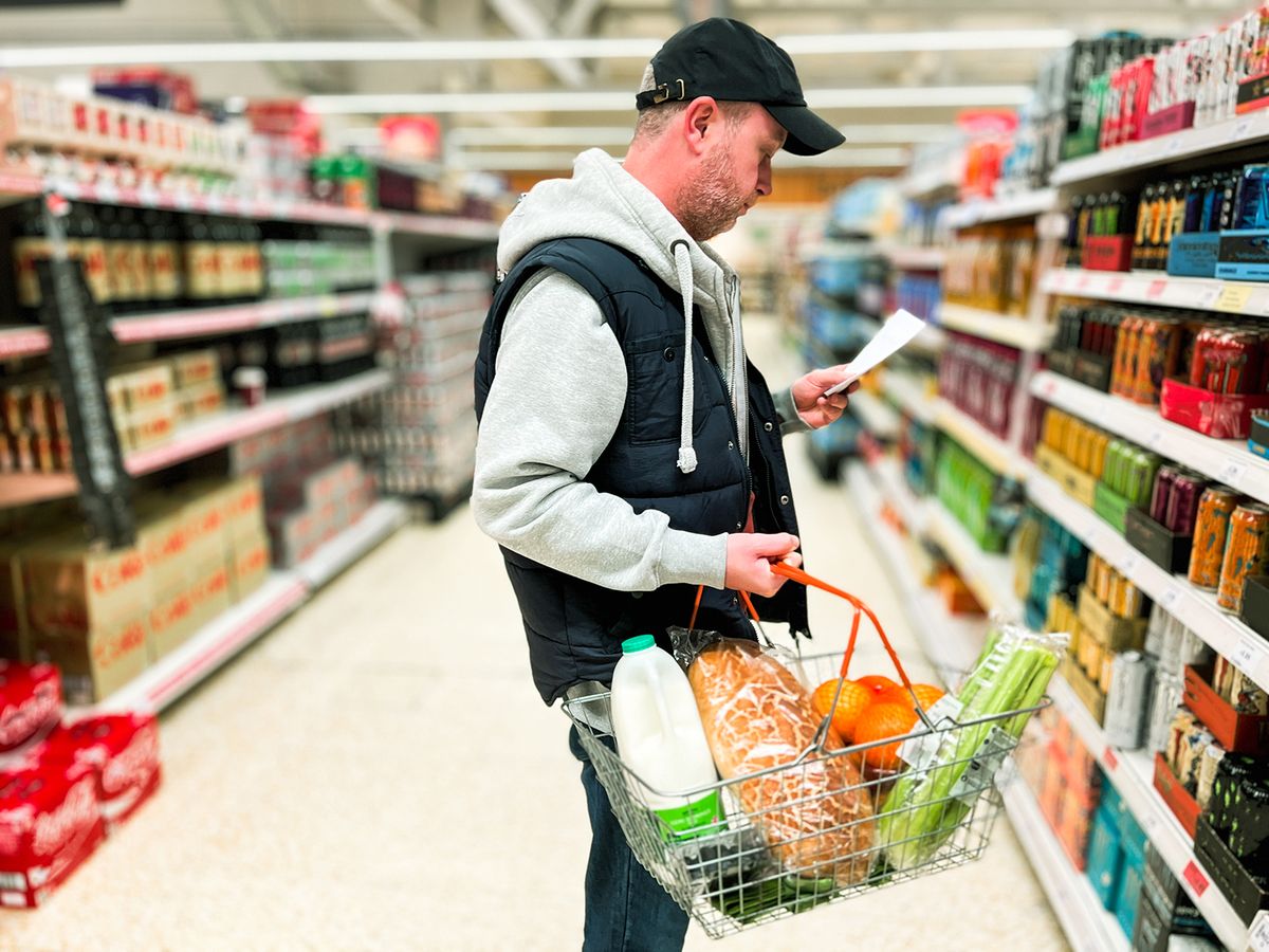 Mid adult man looking at list in energy drink aisle of supermarket