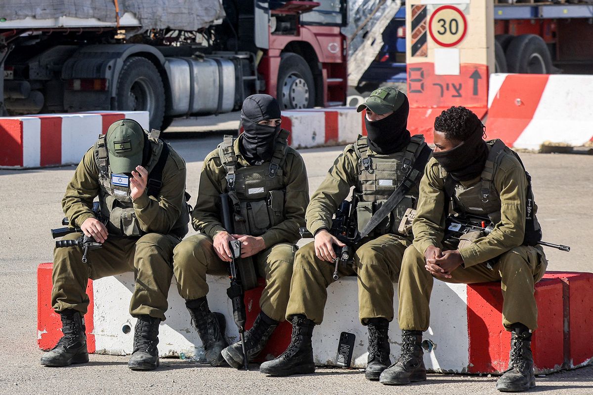 Israeli army soldiers sit together near one of the Egyptian trucks bringing in humanitarian aid supplies to the Gaza Strip, on the Israeli side of the Kerem Shalom border crossing with the Palestinian territory on February 6, 2024, as right-wing Israeli protesters gather to block the trucks from entering amid the ongoing conflict between Israel and the Palestinian militant group Hamas. (Photo by Menahem KAHANA / AFP)