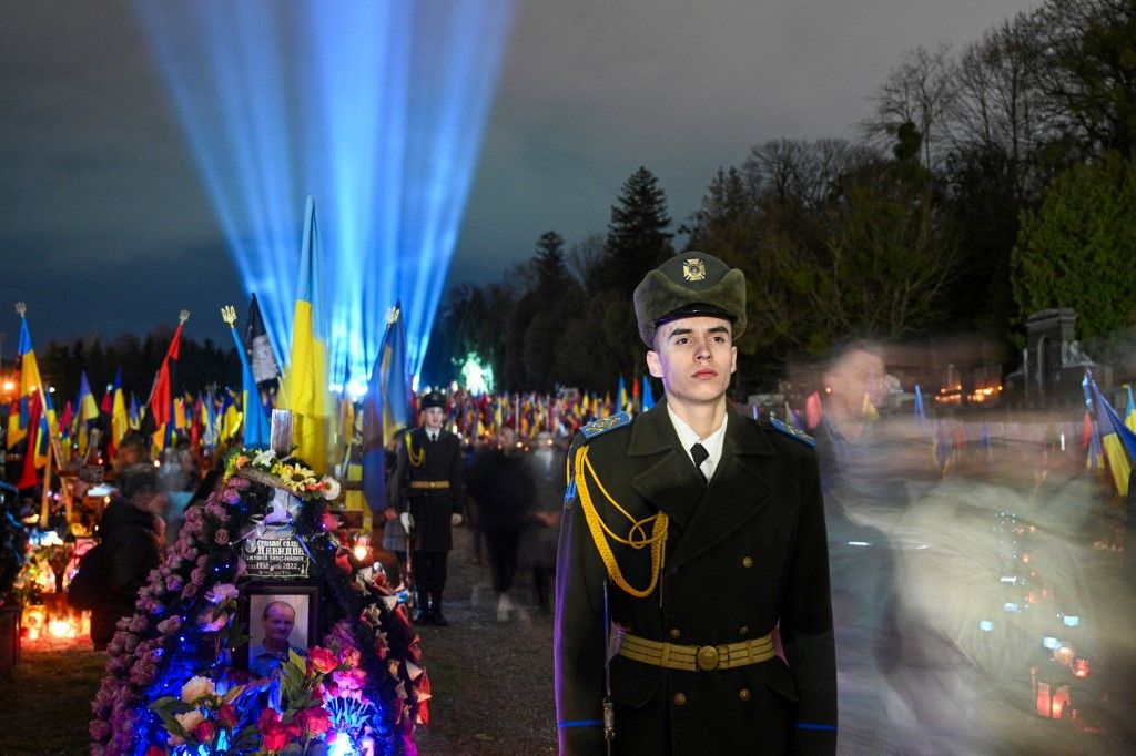 Ukrainian honour guards stand as a symbolic illumination called "Ray of Memory" is seen over the graves of Ukrainian soldiers, who died in the war with Russia, at Lychakiv Cemetery in Lviv on February 23, 2024, on the second anniversary of Russia's invasion of Ukraine. (Photo by YURIY DYACHYSHYN / AFP)