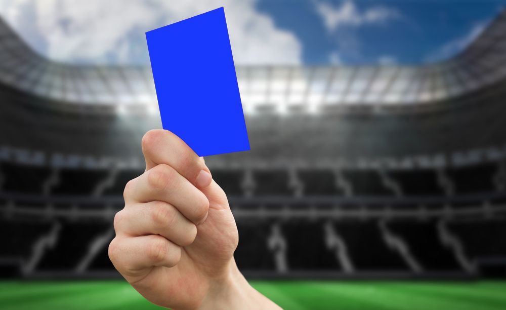 Hand,Holding,Up,Red,Card,Against,Large,Football,Stadium,WithHand holding up red card against large football stadium with empty stands