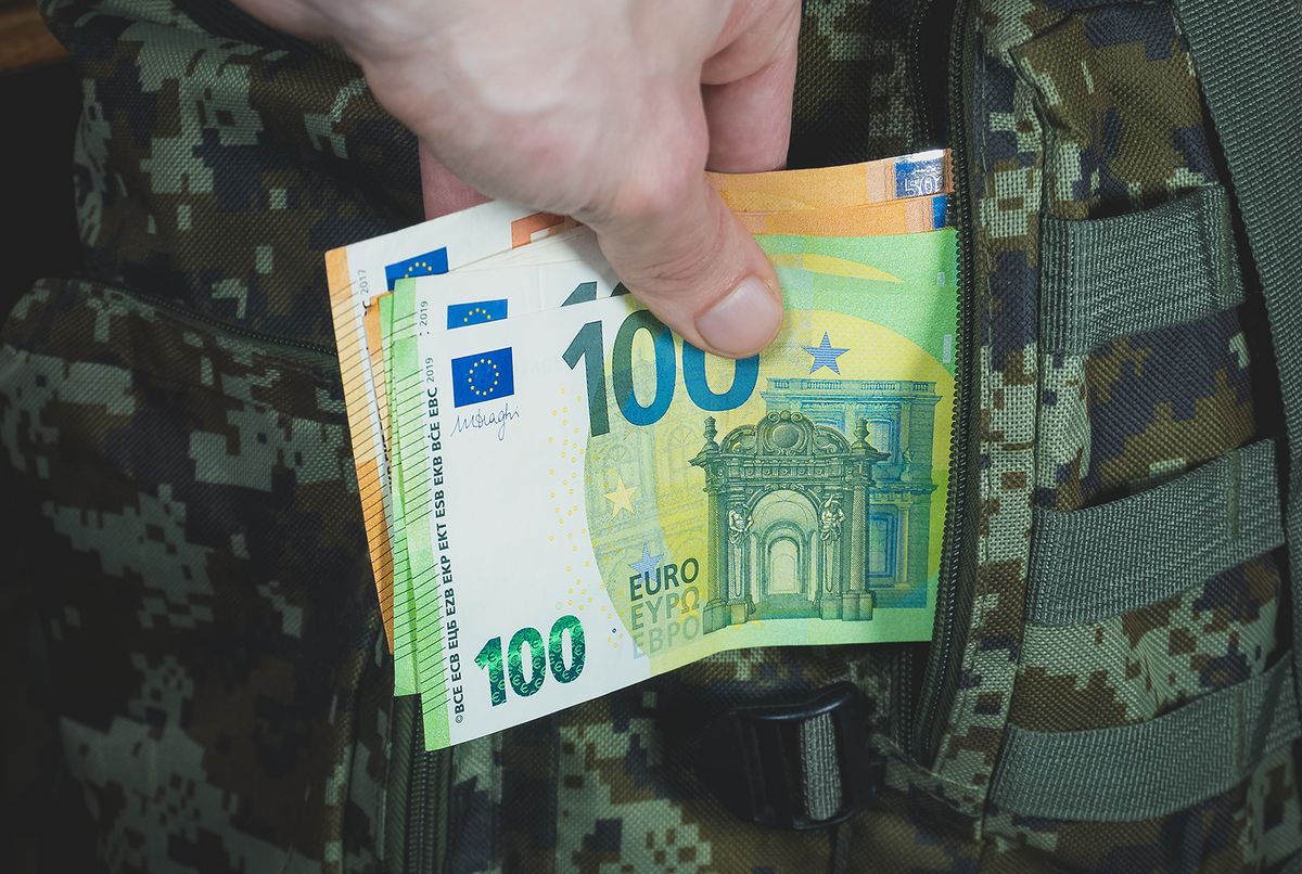 Man is putting in a military backpack euros. Dark green Camouflage khaki bag with money. Migrants and Refugees concept. Looting and Robbery.