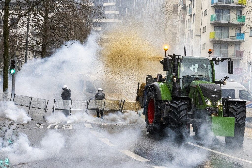 A farmer emits hay from his tractor onto Belgian riot police officers as gas rises from tear gas canisters during a protest called by the farmers' organizations "Federation Unie de Groupements d'Eleveurs et d'Agriculteurs" (FUGEA), Boerenforum and MAP, in response to the European Agriculture Council, in Brussels, on February 26, 2024. Farmers across Europe have been protesting for weeks over what they say are excessively restrictive environmental rules, competition from cheap imports from outside the European Union and low incomes. (Photo by NICOLAS MAETERLINCK / BELGA / AFP) / Belgium OUT
