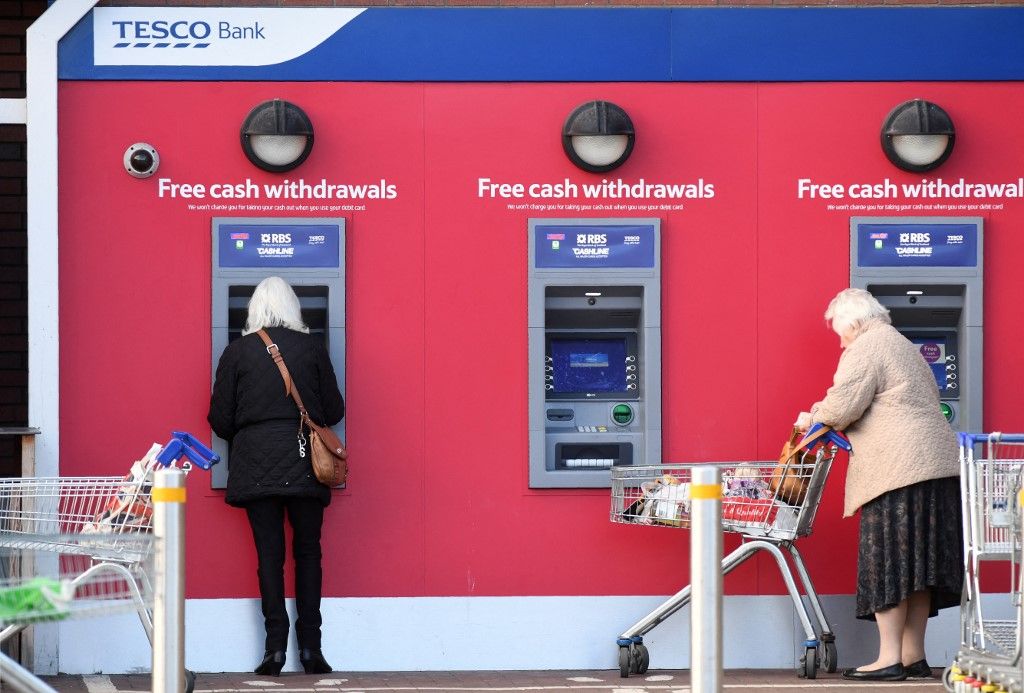 Customers use RBS branded automated teller machines (ATMs), at a Tesco Bank cash point, in Liverpool, north west England, on November 7, 2016. Britain's Tesco Bank said Monday that around 20,000 customers had money stolen from their accounts after it was hit by hackers. The bank, a subsidiary of British supermarket giant Tesco, the UK's biggest retailer, said it was trying to refund accounts that had been subject to fraud as quickly as possible. (Photo by PAUL ELLIS / AFP)