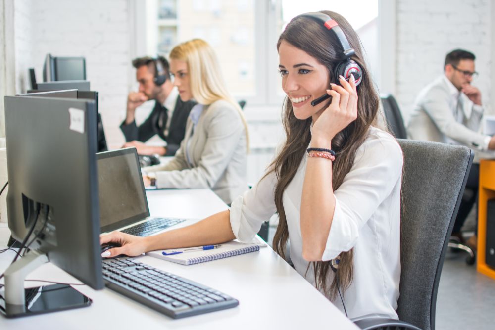 Friendly,Smiling,Woman,Call,Center,Operator,With,Headset,Using,Computer