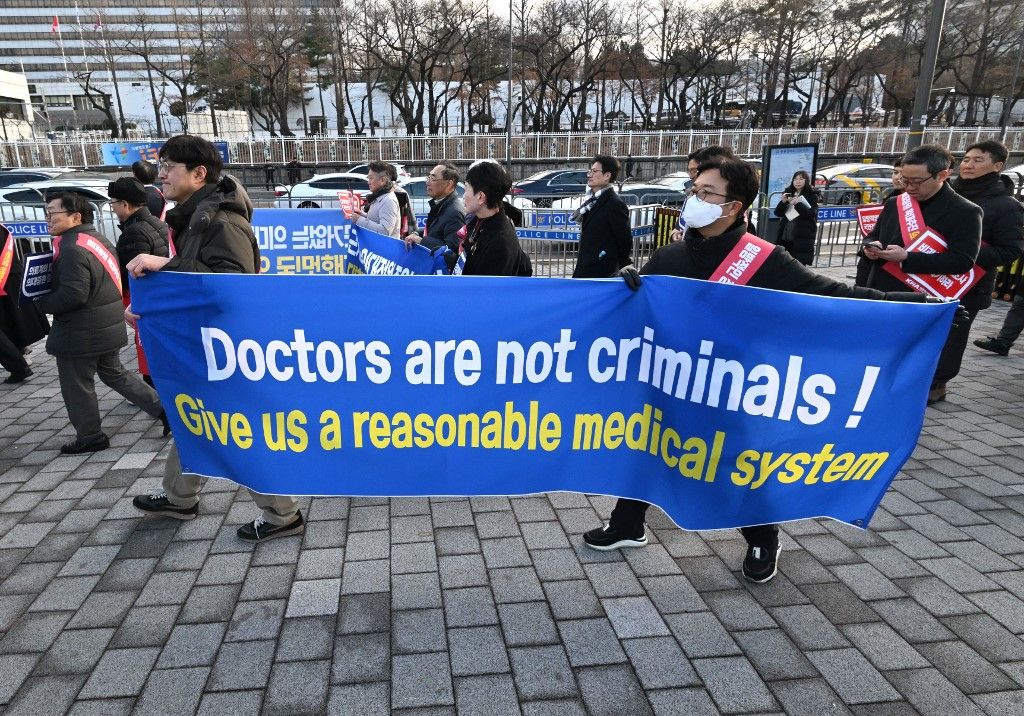 Doctors carry a banner reading "Doctors are not criminals!" as they march toward the Presidential Office during a rally to protest against the government’s plan to raise the annual enrolment quota at medical schools, in Seoul on February 25, 2024. South Korea has raised its public health alert to the highest level, authorities announced on February 23, saying health services were in crisis after thousands of doctors resigned over proposed medical reforms. (Photo by Jung Yeon-je / AFP)