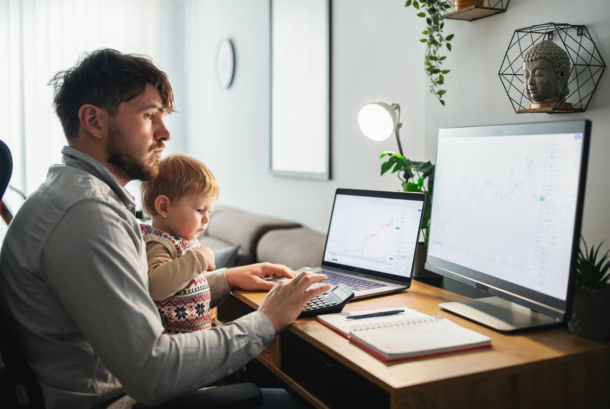 Man trading on his computer from his home office while taking care of his son.
