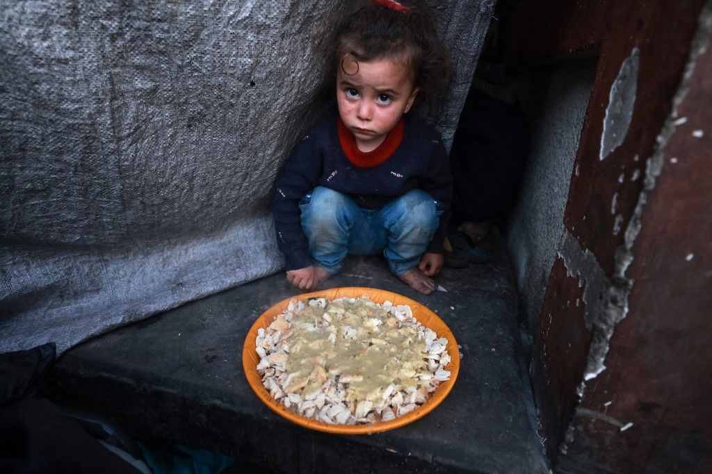 A Palestinian child sits next to a plate before an "iftar" meal, the breaking of fast, on the second day of the Muslim holy fasting month of Ramadan, at a shelter for displaced people in Rafah in the southern Gaza Strip on March 12, 2024, amid ongoing battles between Israel and the militant group Hamas. (Photo by MOHAMMED ABED / AFP)