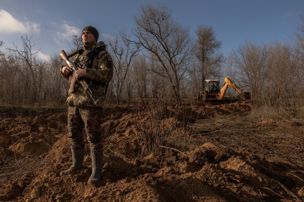 A Ukrainian serviceman stands guard checking for Russian drones in the sky as a soldier in a tractor digs a trench system in the Zaporizhzhia region, on January 30, 2024, amid the Russian invasion of Ukraine. After Kyiv's counter-offensive failed to punch through Russian lines last year, Kyiv has switched to the defensive -- building up its own lines of protection to thwart a possible Russian offensive. No side has made a significant territorial gain in more than a year, but fighting has remained intense. For Ukraine, building trenches marks a radical change in approach. The stronger each side's defensive positions become, the greater the risk is that the front lines stay static and the conflict turns frozen. That would complicate Kyiv's objective of liberating the approximately 20 percent of its territory under Russian control. (Photo by Roman PILIPEY / AFP)