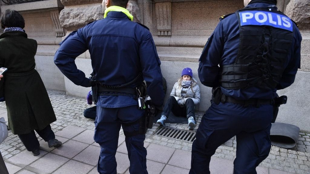 Swedish climate activist Greta Thunberg (C) looks at policemen as she sits outside the Swedish parliament, the Riksdagen, to demonstrate for climate action, on March 12, 2024 in Stockholm, Sweden. (Photo by Samuel STEEN / TT News Agency / AFP) / Sweden OUT