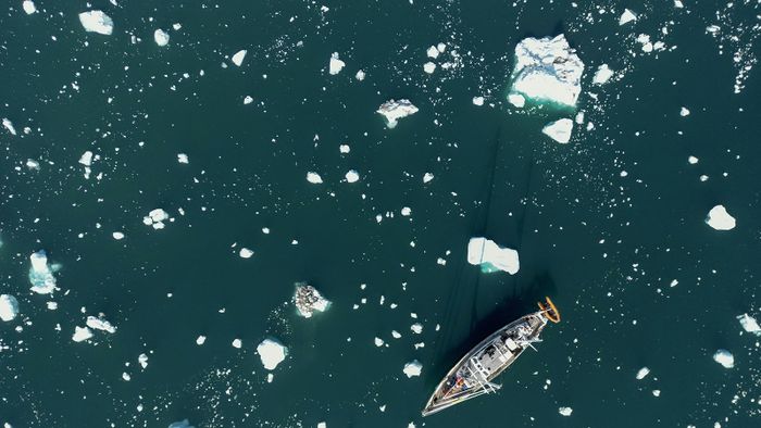 Egy tudományos expedíciós vitorlás, a Kamak olvadó jéghegyek töredékei között navigál a grönlandi Scoresby-fjordban 2023. augusztus 16-án.  The French National Centre for Scientific Research (CNRS) is undertaking an expedition to explore Greenland's isolated fjords, the planet's largest fjord system, which remains vastly understudied. The expedition, arranged by the volunteer-run French initiative Greenlandia, is dedicated to understanding the climate change's effects on Scoresby Fjord and its inhabitants. (Photo by Olivier MORIN / AFP)