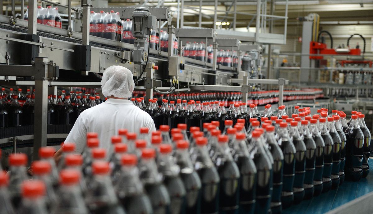 An employee is pictured next to the production line in the bottling plant of the Coca-Cola Erfrischungsgetränke AG production facility in Genshagen, Germany, 21 August 2013. Here, Coca-Cola products are filled into disposable packaging on 158,000 square meters. 170 employees work in the production facility, which was opened in 1998. The Coca-Cola Erfrischungsgetränke AG is one of the biggest beverage companies in Germany with a sales volume of 3.7 billion liters in 2012. Photo: Jens Kalaene (Photo by JENS KALAENE / ZB / dpa Picture-Alliance via AFP)