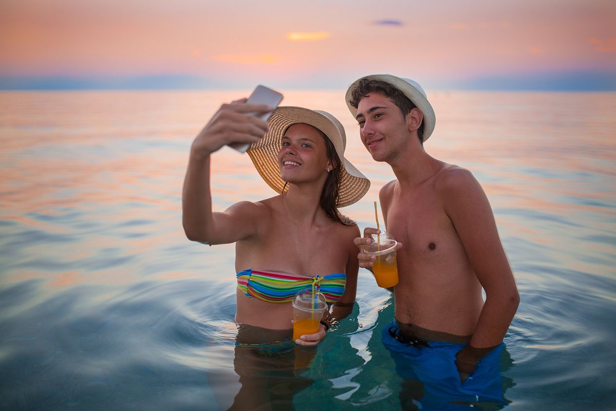 Young couple taking selfie photograph using smartphone on the beach