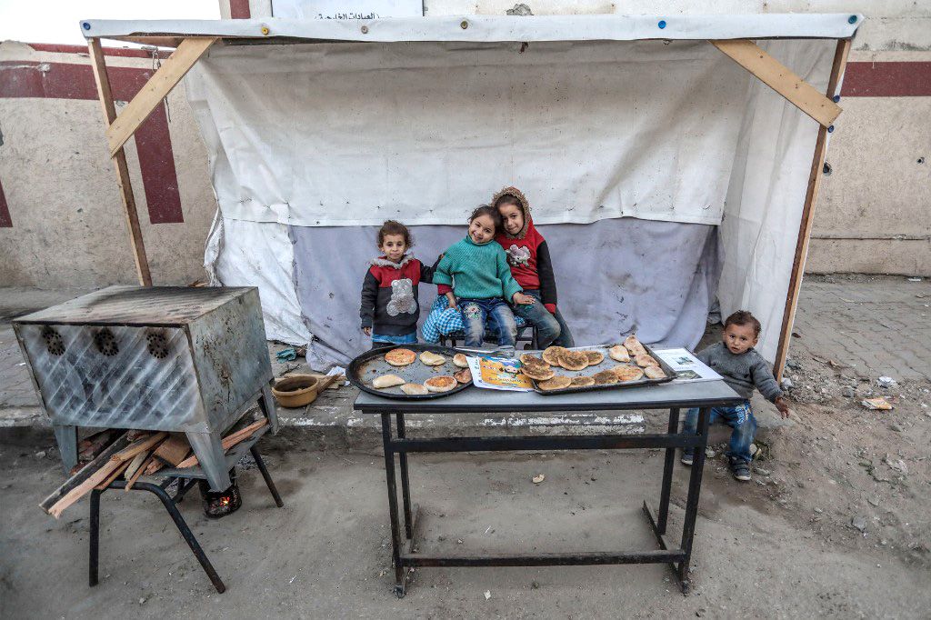 PALESTINIAN-ISRAEL-CONFLICTChildren pose for a picture at a stand selling flatbread in Deir al-Balah in central Gaza on March 3, 2024, amid the ongoing battles between Israel and the Palestinian militant Hamas group. (Photo by AFP)