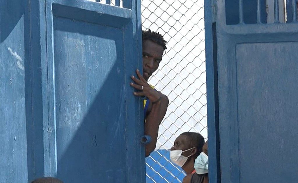 This screen grab taken from AFPTV shows a person looking out from behind a door near the main prison of Port-au-Prince, Haiti, on March 3, 2024, after a breakout by several thousand inmates. At least a dozen people died as gang members attacked the main prison in Haiti's capital, triggering a breakout by several thousand inmates, an AFP reporter and an NGO said on March 3. "We counted many prisoners' bodies," said Pierre Esperance of the National Network for Defense of Human Rights, adding that only around 100 of the National Penitentiary's estimated 3,800 inmates were still inside the facility after the gang assault overnight on March 2. (Photo by Luckenson JEAN / AFPTV / AFP)