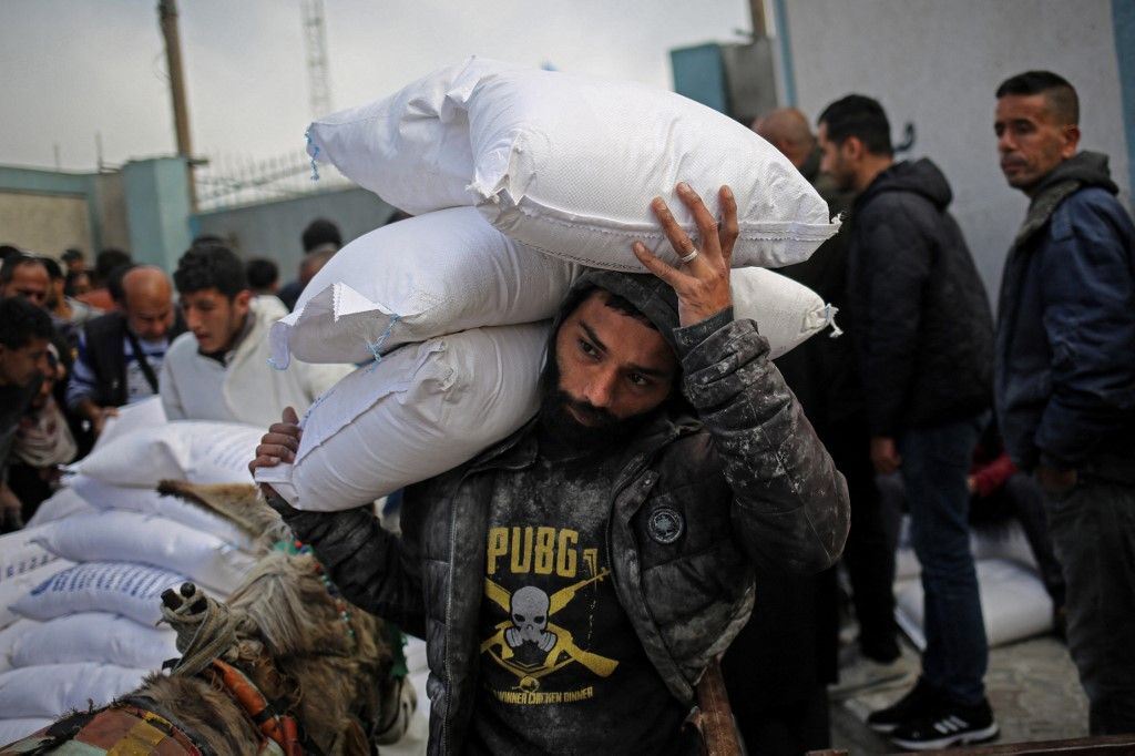 A Palestinian man carries sacks of humanitarian aid at the distribution center of the United Nations Relief and Works Agency for Palestine Refugees (UNRWA), in Rafah in the southern Gaza Strip on March 3, 2024, amid the ongoing conflict between Israel and the Hamas movement. (Photo by AFP)