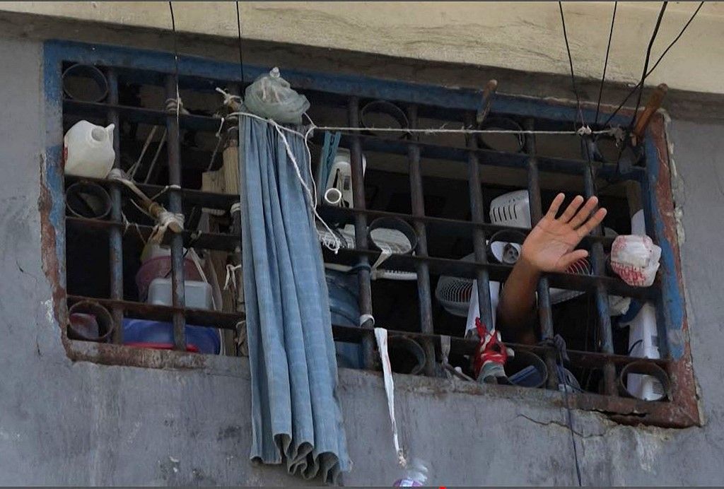This screen grab taken from AFPTV shows a person waving his hand from a cell inside the main prison of Port-au-Prince, Haiti, on March 3, 2024, after a breakout by several thousand inmates. At least a dozen people died as gang members attacked the main prison in Haiti's capital, triggering a breakout by several thousand inmates, an AFP reporter and an NGO said on March 3. "We counted many prisoners' bodies," said Pierre Esperance of the National Network for Defense of Human Rights, adding that only around 100 of the National Penitentiary's estimated 3,800 inmates were still inside the facility after the gang assault overnight on March 2. (Photo by Luckenson JEAN / AFPTV / AFP)