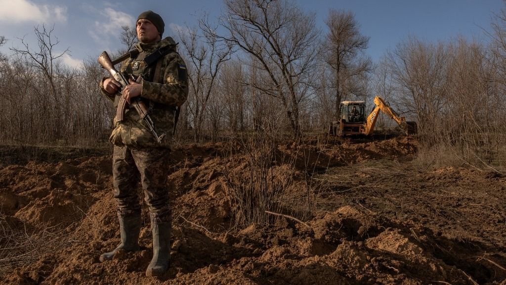 A Ukrainian serviceman stands guard checking for Russian drones in the sky as a soldier in a tractor digs a trench system in the Zaporizhzhia region, on January 30, 2024, amid the Russian invasion of Ukraine. After Kyiv's counter-offensive failed to punch through Russian lines last year, Kyiv has switched to the defensive -- building up its own lines of protection to thwart a possible Russian offensive. No side has made a significant territorial gain in more than a year, but fighting has remained intense. For Ukraine, building trenches marks a radical change in approach. The stronger each side's defensive positions become, the greater the risk is that the front lines stay static and the conflict turns frozen. That would complicate Kyiv's objective of liberating the approximately 20 percent of its territory under Russian control. (Photo by Roman PILIPEY / AFP)