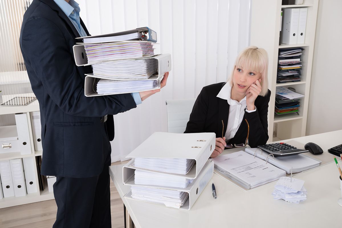 Businessman,Giving,Pile,Of,Folders,To,Young,Female,Assistant,In