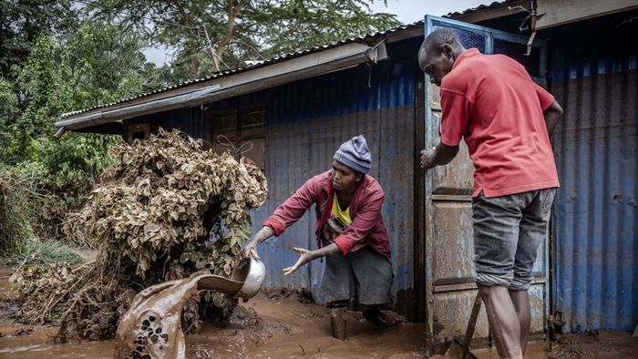Egy nő és egy férfi sarat és vizet hord ki a házukból Mai Mahiuban.