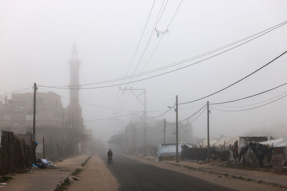 A Palestinian man pushes a child in a wheelchair on a roadside amid thick fog in Rafah in the southern Gaza Strip early morning on April 4, 2024, amid the ongoing conflict between Israel and the militant group Hamas. (Photo by MOHAMMED ABED / AFP)
