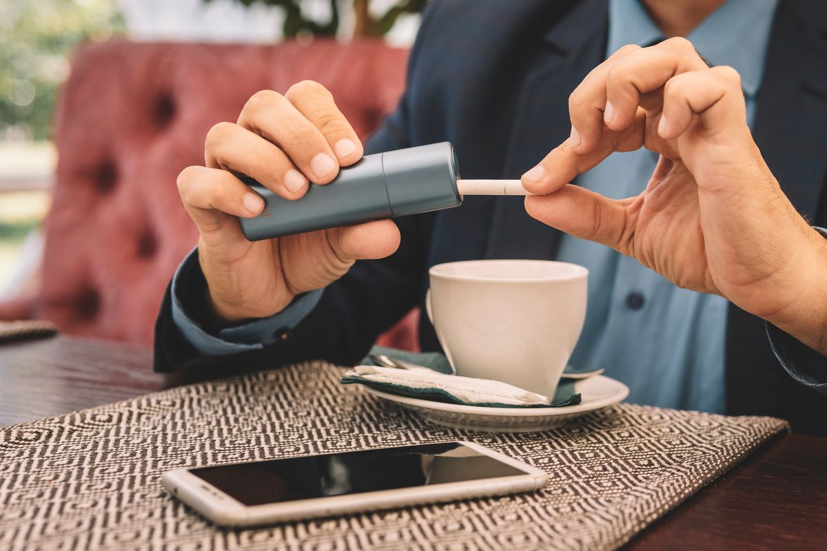 man fills gadget with a cigarette. new smoking technology. Smoker smoking hybrid smokeless cigarette device that uses real tobacco refills, hybrid technology between analog and electronic cigarettes.