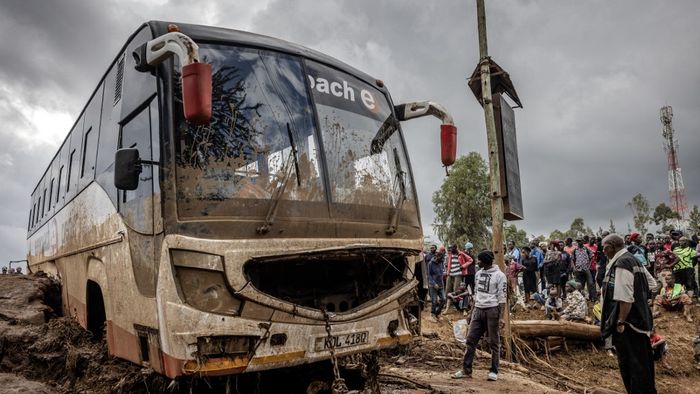Az emberek egy megsérült busz mellett gyülekeznek Mai Mahiuban, amelyet elsodort a víz heves esőzések és hirtelen áradások által erősen sújtott területen. 