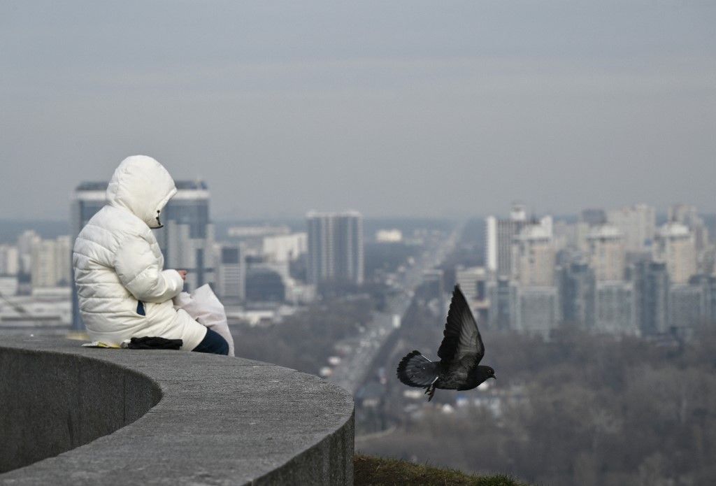 A pigeon flies by a woman sitting in a park in Kyiv, on February 26, 2024, amid the Russian invasion of Ukraine. (Photo by Genya SAVILOV / AFP)