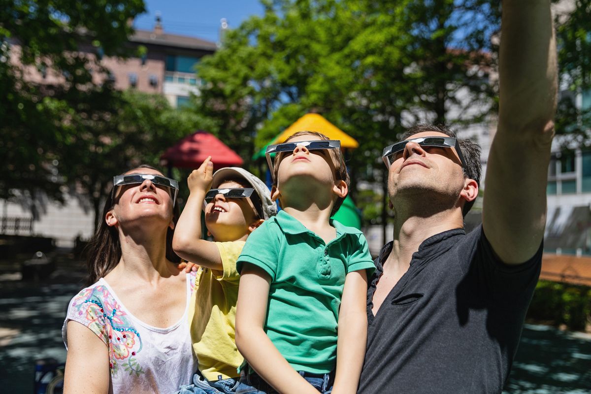 All the family look at solar eclipse in the city street in a public park