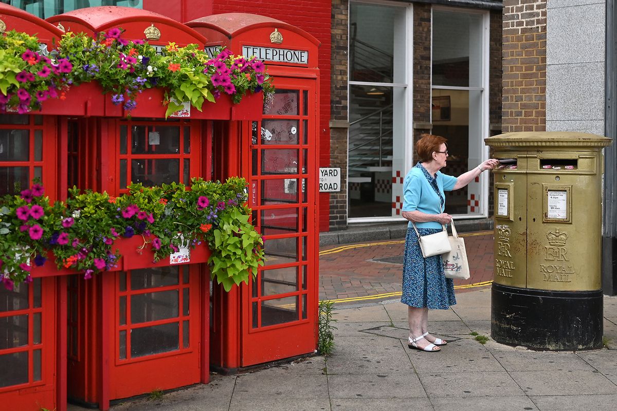 posta A person posts a letter in a golf Royal Mail post box, alongside florally decorated red telephone boxes the High Street in Uxbridge, west London on July 11, 2023. In the Conservative stronghold of Uxbridge, west London, many voters hope that change is in the air as they prepare to choose former prime minister Boris Johnson's replacement as MP. Johnson quit parliament last month and the opposition Labour Party is favourite to pick up the seat when voters go to the polls on July 20. (Photo by Justin TALLIS / AFP) / TO GO WITH AFP STORY BY Caroline TAIX