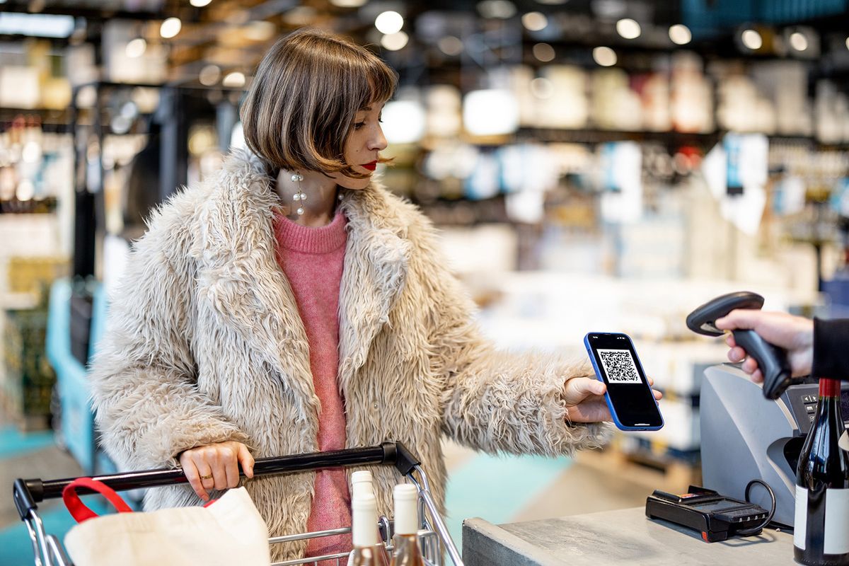 Woman pays with a QR code or scans her loyalty card on phone at a supermarket checkout. Concept of modern retailing technologies in supermarket