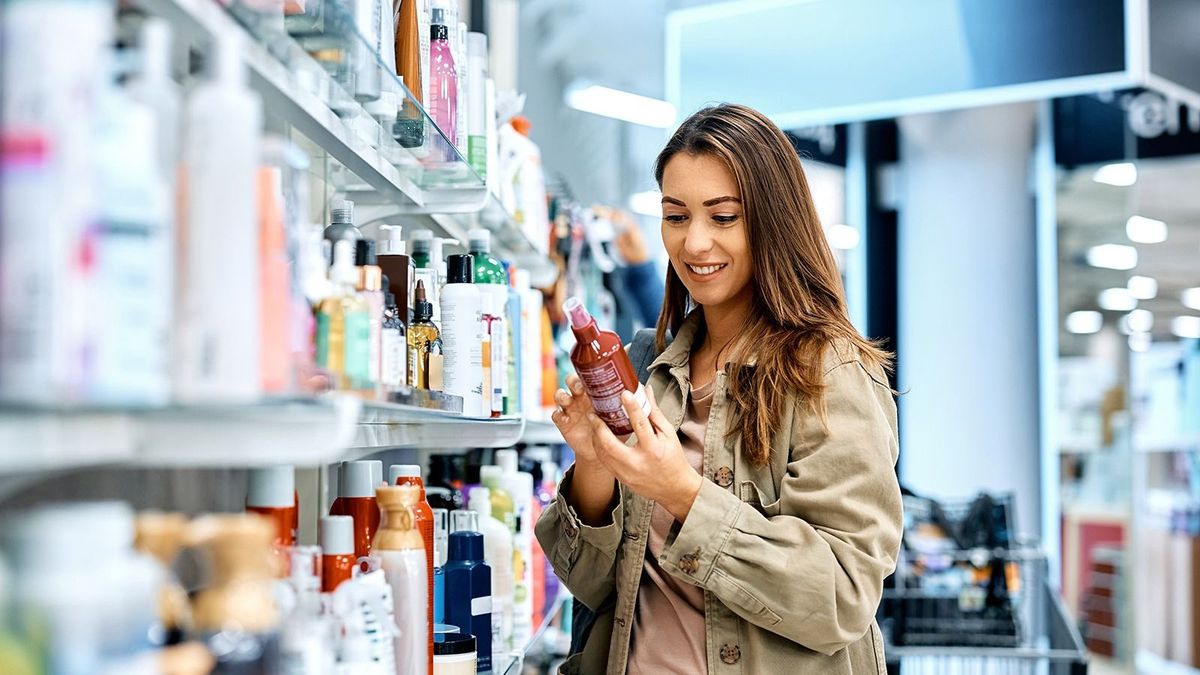 Young happy woman reading ingredients of skin care product while shopping at the store.