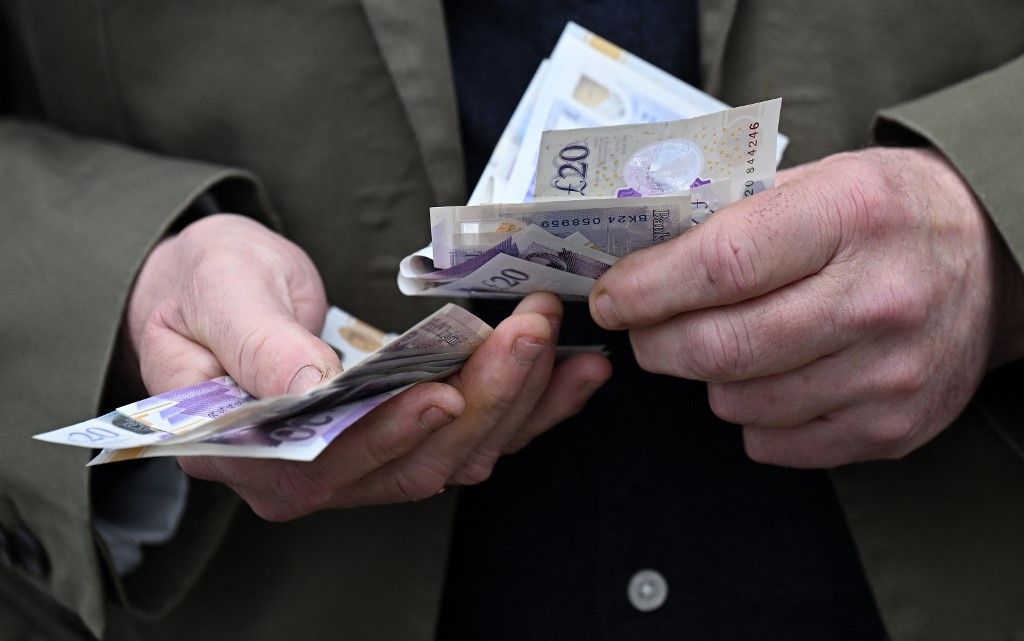 A bookmaker handles a wad of pound notes as racegoers place bets at a betting stand ahead of racing on the final day of the Grand National Festival horse race meeting at Aintree Racecourse in Liverpool, north-west England, on April 13, 2024. (Photo by Paul ELLIS / AFP)