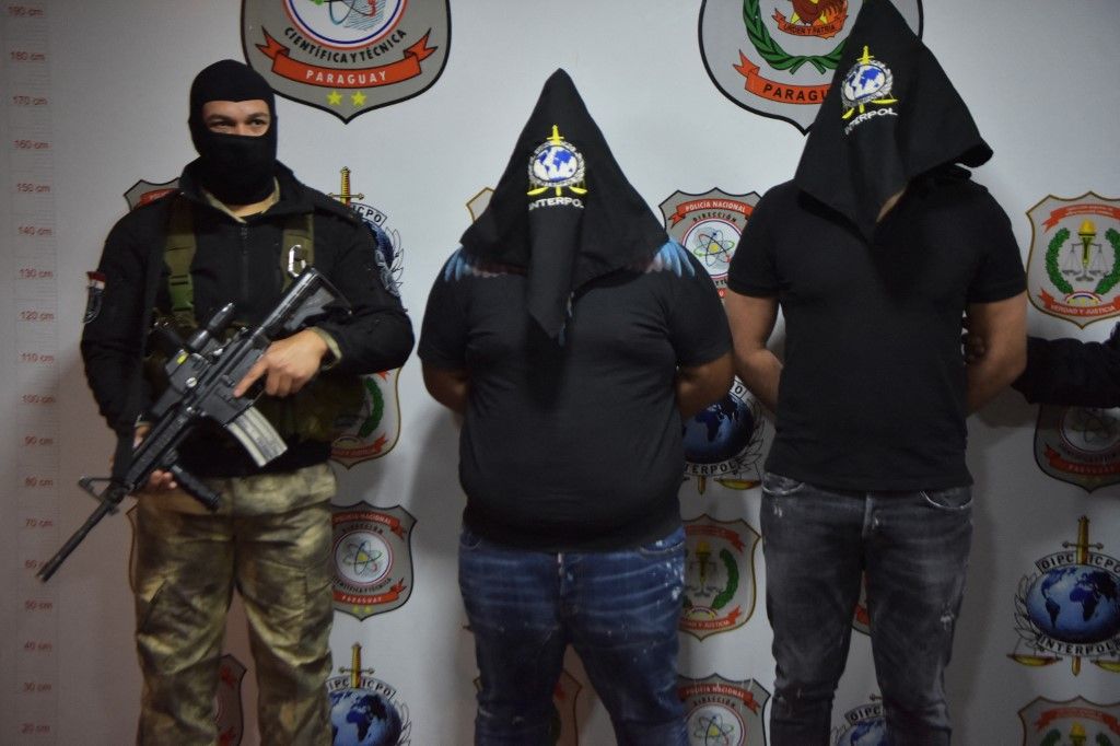 Two Italian cousins named the same, Giuseppe Giorgi, are shown to the press with their faces covered by Interpol officers in Asuncion on July 14, 2023. Two alleged members of the 'Ndrangheta mafia, wanted by the Italian Interpol, were arrested in Asuncion and will be turned over to Italy. (Photo by NORBERTO DUARTE / AFP) maffia