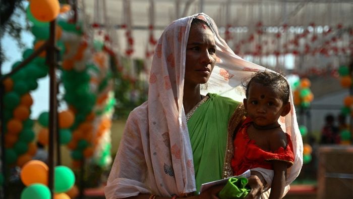 Egy szavazó gyermekével együtt arra vár, hogy leadhassa szavazatát egy szavazóhelyiség előtt az indiai általános választások szavazásának első szakaszában, Dugeli faluban