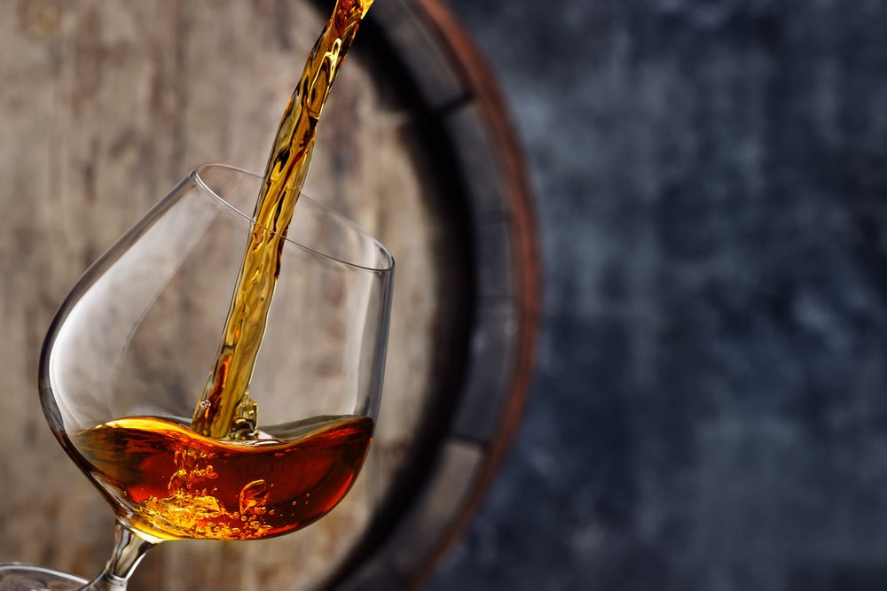 Brandy,Pouring,Into,Glass,And,Old,Wooden,Barrel,As,Background