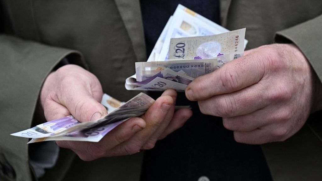 A bookmaker handles a wad of pound notes as racegoers place bets at a betting stand ahead of racing on the final day of the Grand National Festival horse race meeting at Aintree Racecourse in Liverpool, north-west England, on April 13, 2024. (Photo by Paul ELLIS / AFP)