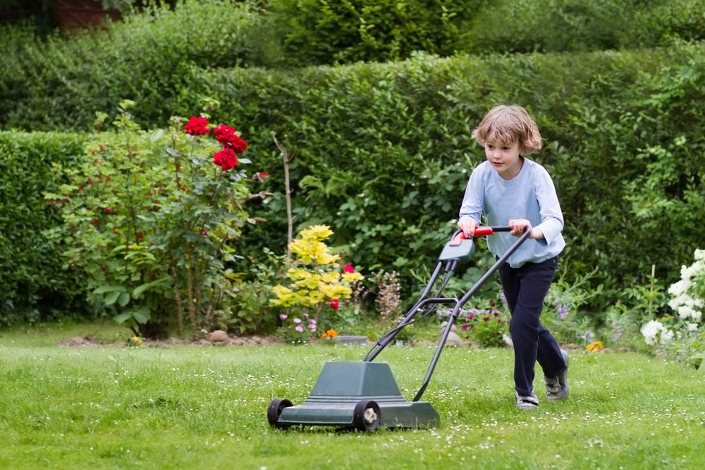 Little,Boy,Playing,With,A,Lawn,Mower,In,The,Garden
