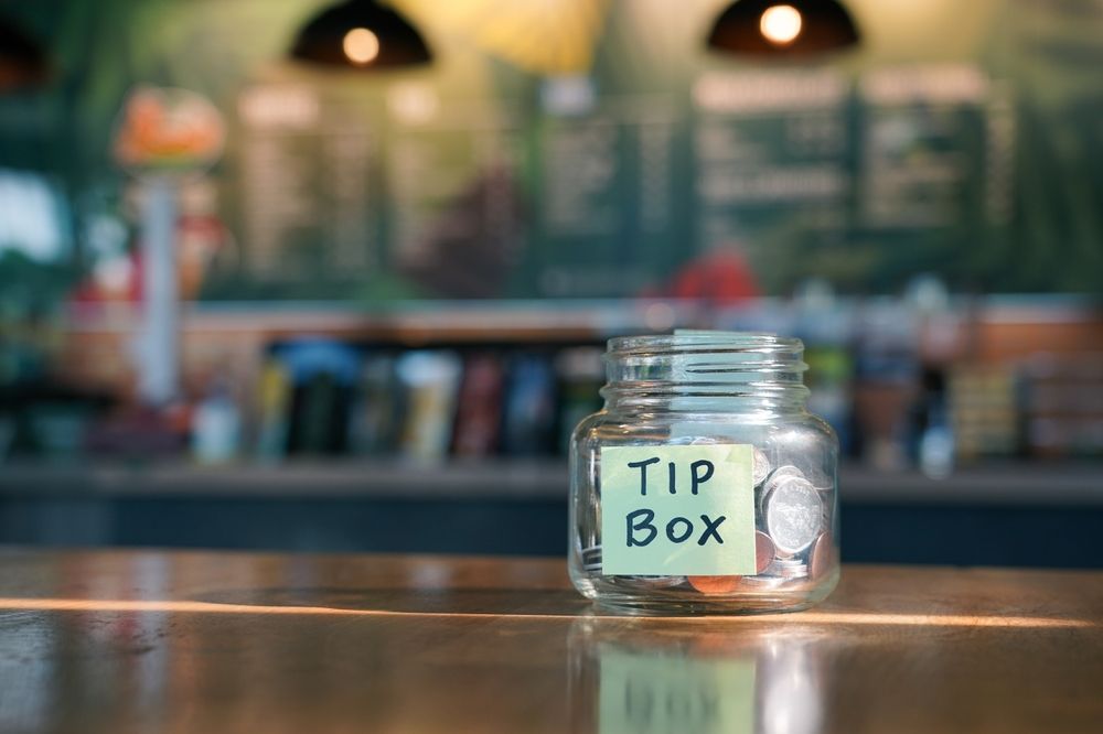 Tip,Box,,Coins,In,Glass,Jar,With,Blurred,Cafe,Background.