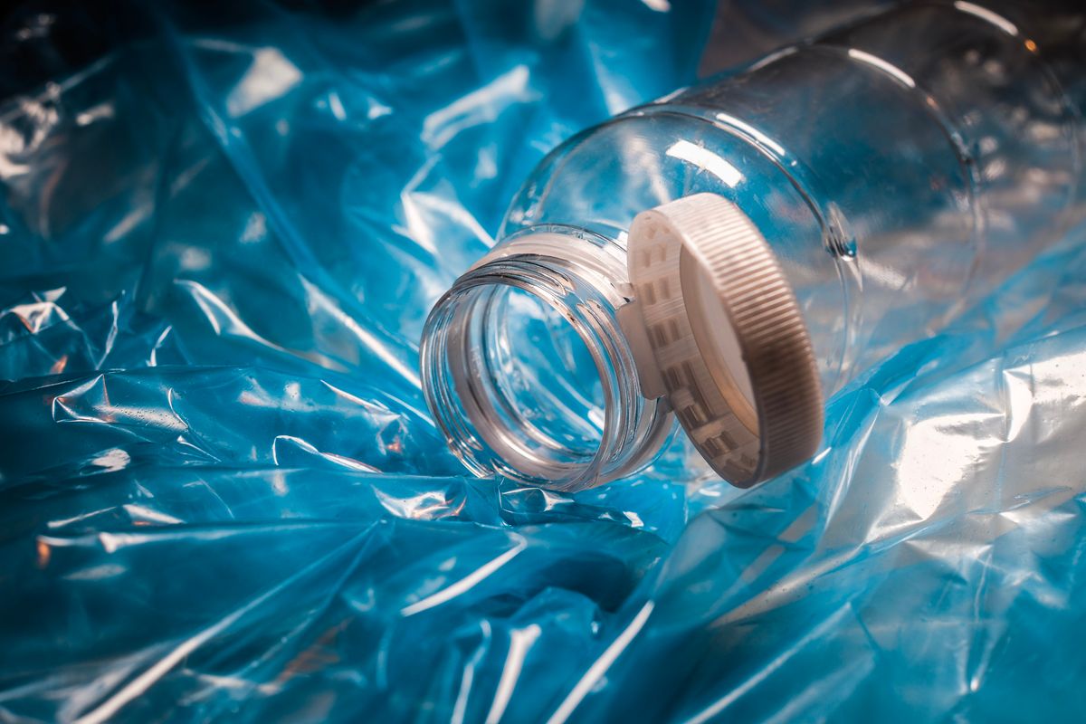 Plastic bottle with cap attached to container, over a garbage