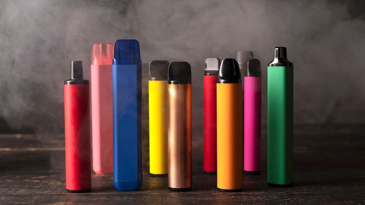 Set of colorful disposable electronic cigarettes on a dark wood background with smoke. The concept of modern smoking, vaping and nicotine.